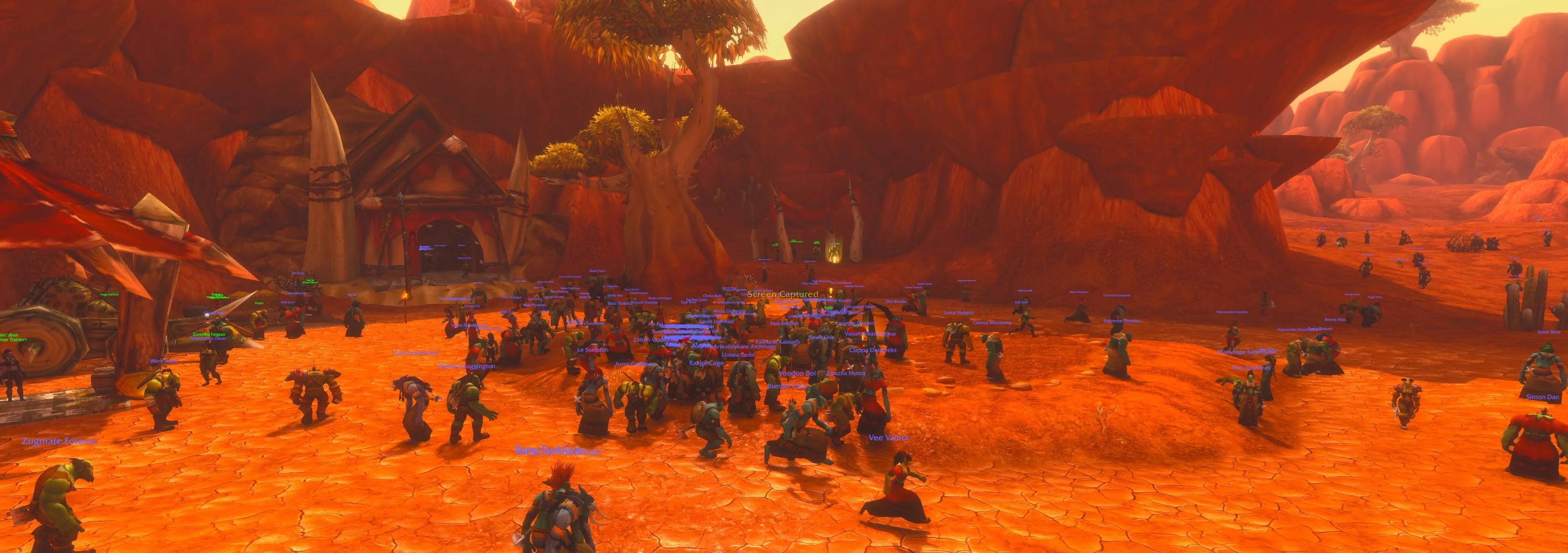 Dozens of orc and troll player characters crowding a red-rock canyon beside a spiked Horde hut, their names floating above them